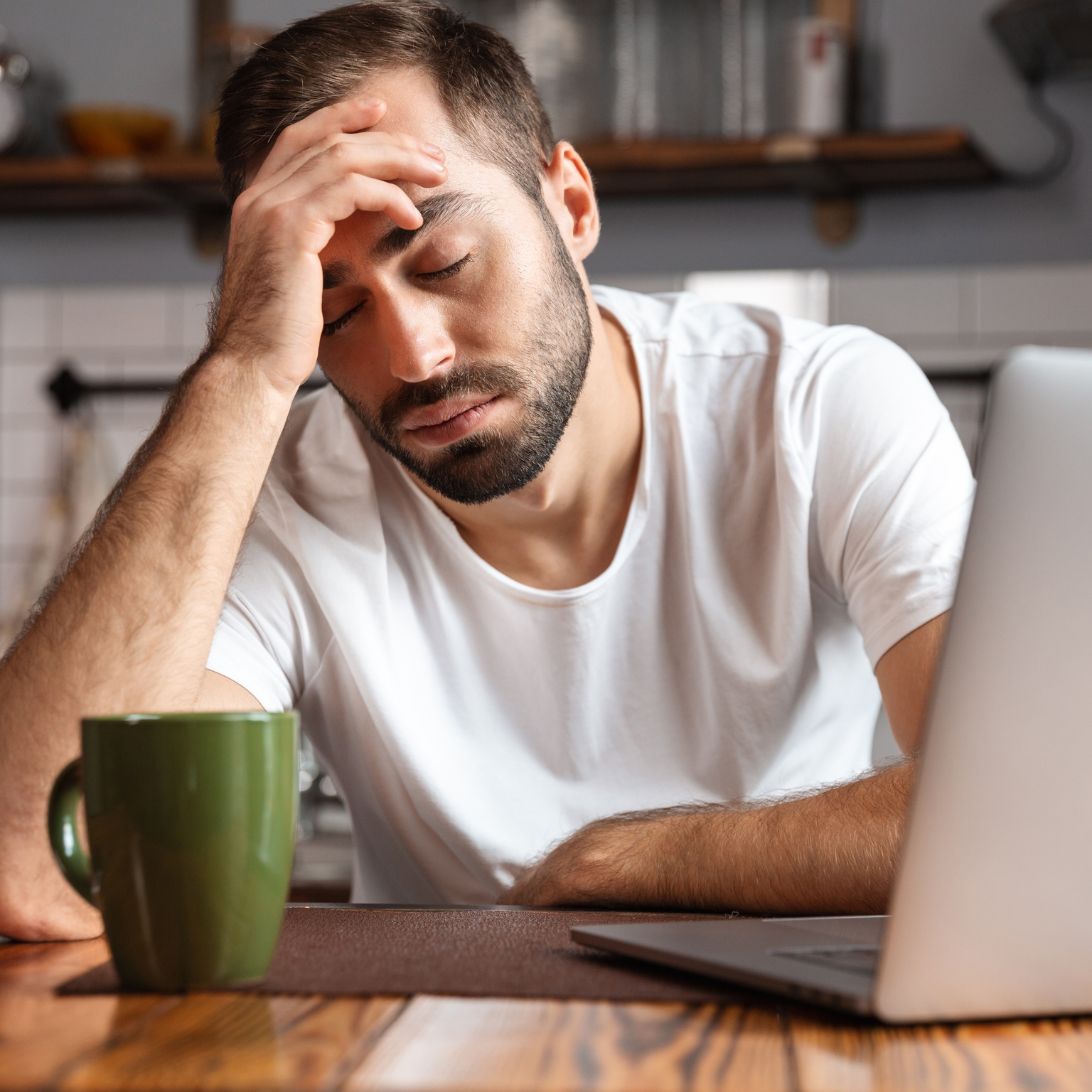 Man met laptop en mok voor zich, ziet er moe uit