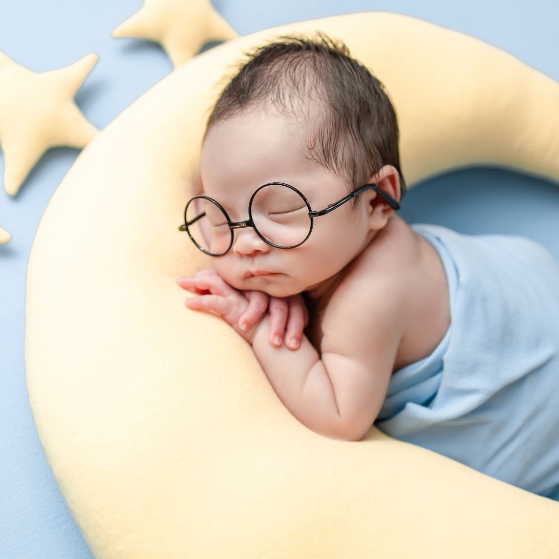 Baby met bril aan het slapen op kussen in de vorm van een halve maan