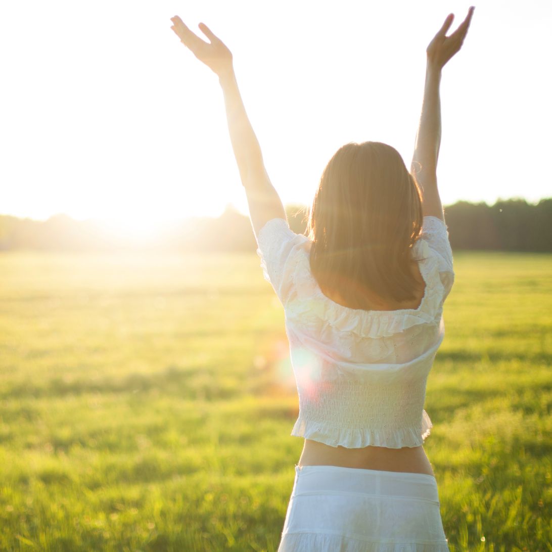 Vrouw staat met armen omhoog richting de zon, neemt meer vitamine D op, een van de manieren om slaapproblemen op te lossen