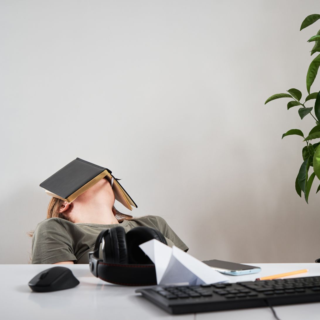 Een student slaapt met een boek op haar hoofd, de afbeelding benadrukt het effect van slaap op examenresultaten