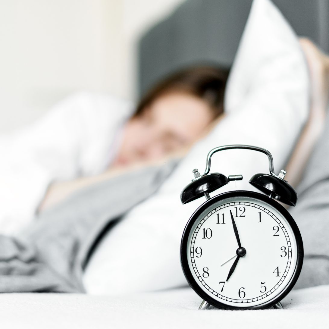 Vrouw met slaaptekort ligt in bed met wekker ernaast