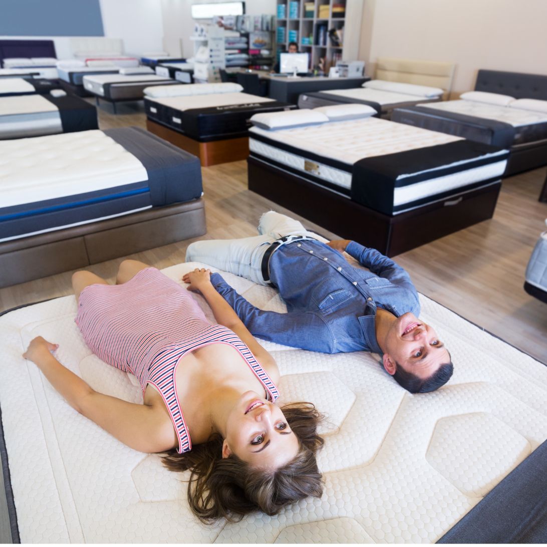 Man en vrouw testen juiste matras hardheid voor rugslapers in winkel