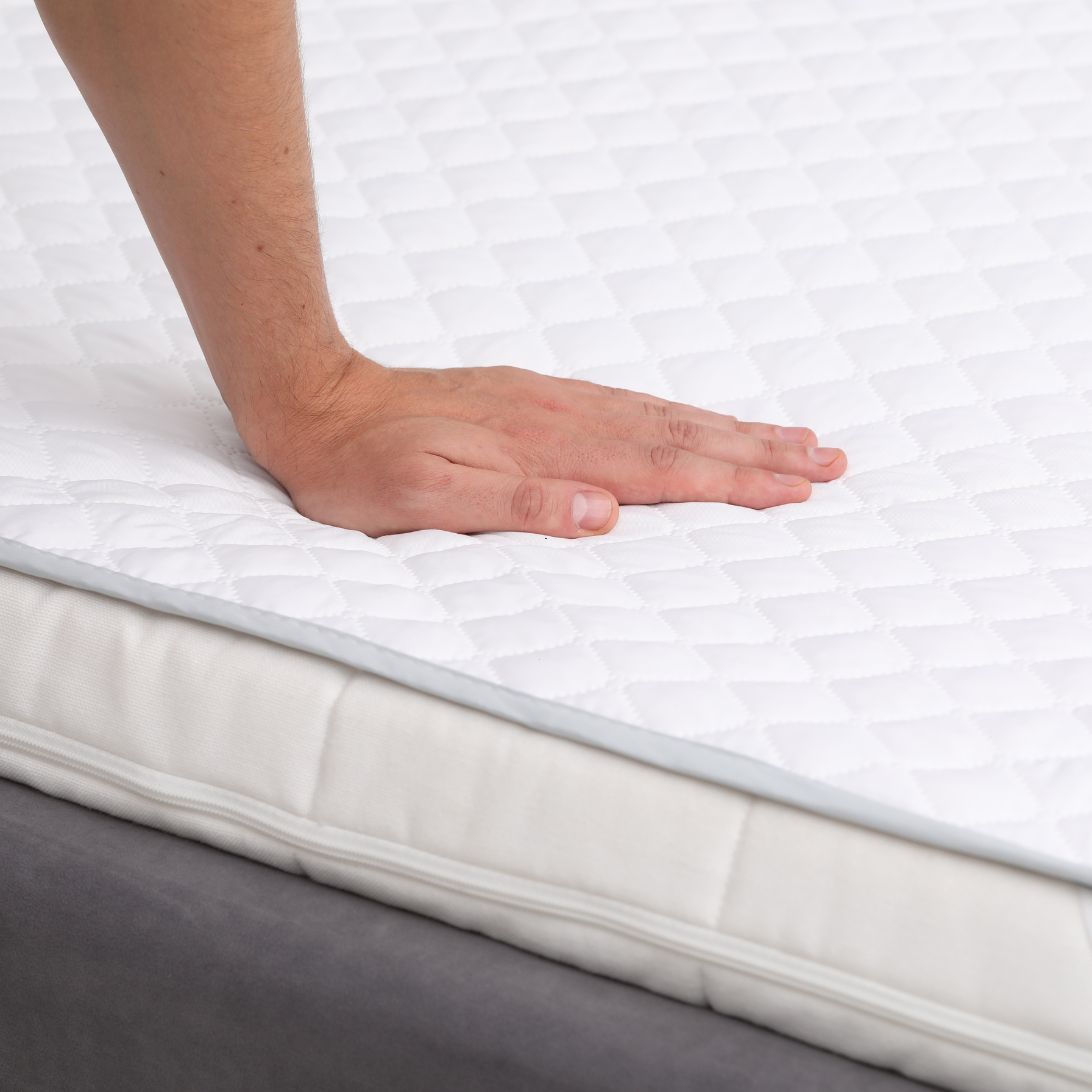 Matrasbeschermer 2 Hand raakt matrasbeschermer aan