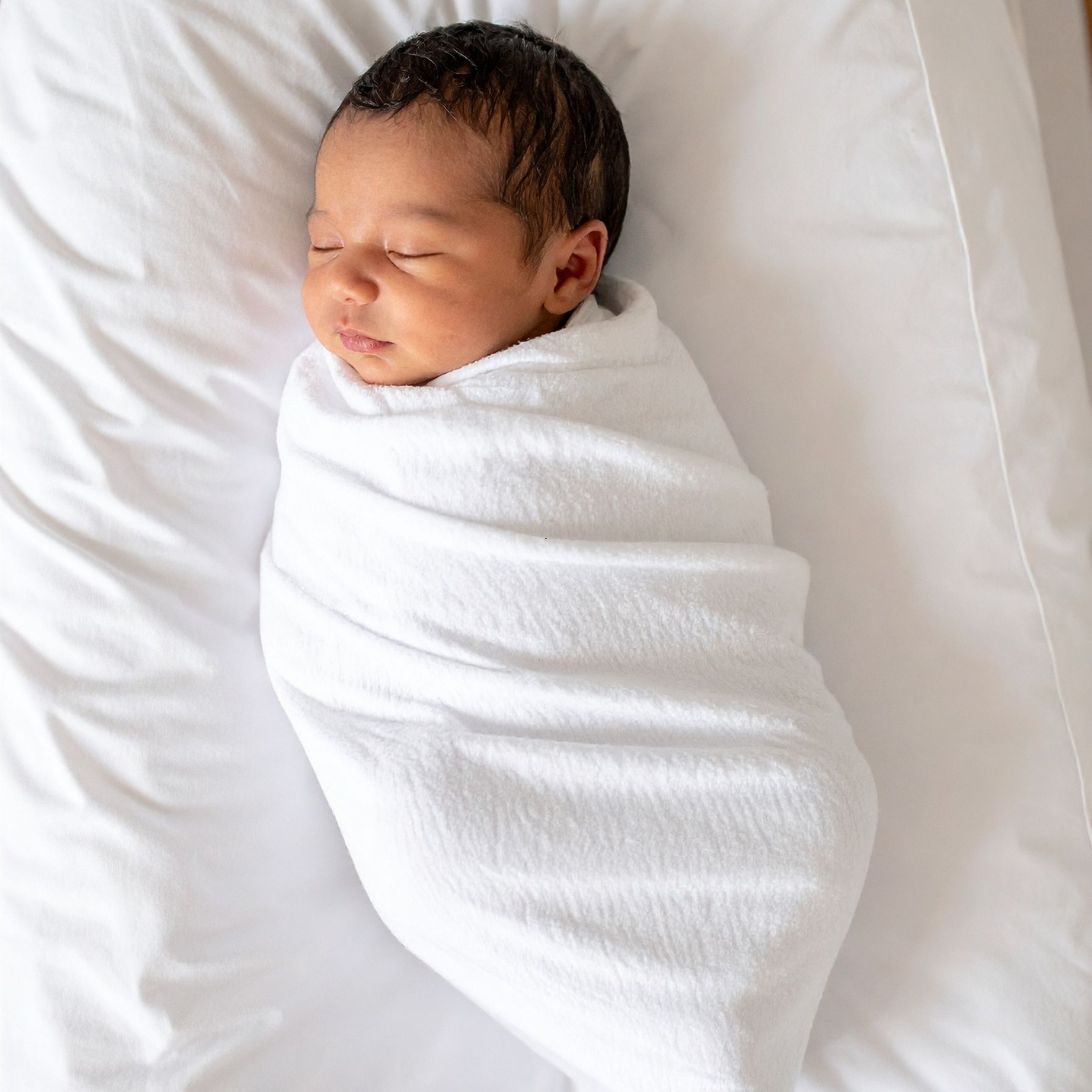 Baby ligt ingewikkeld in dekentje te slapen op babymatras