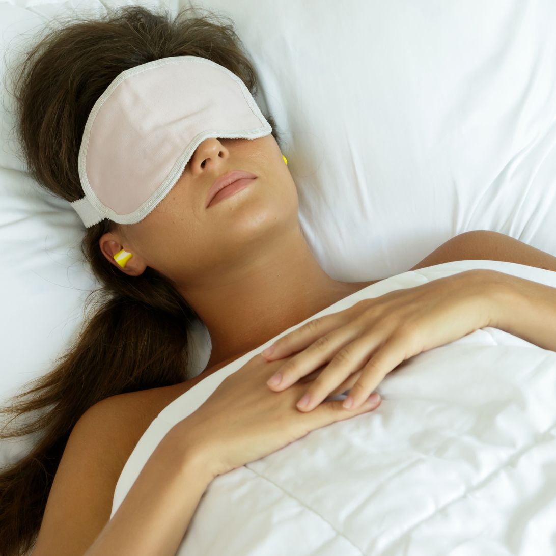 Vrouw ligt in bed te slapen met slaapmasker op en slaap-oordoppen in